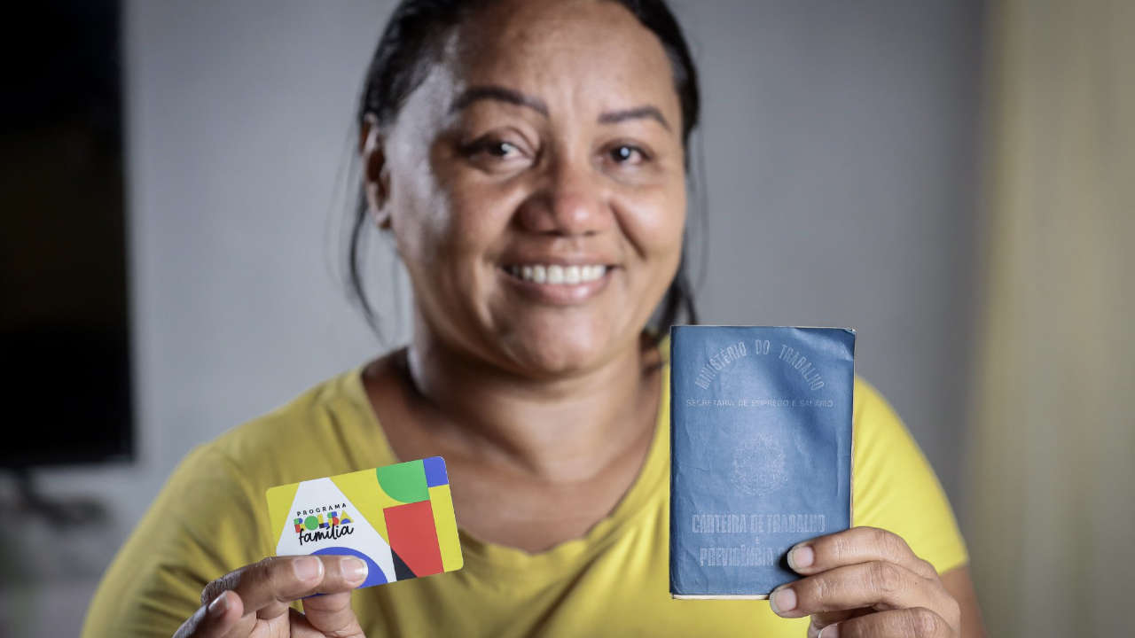 Mulher segurando o cartão do Bolsa Família e Carteira de Trabalho