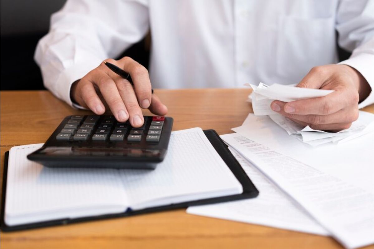 Uma pessoa com sua nota no fiscal e fazendo um cálculo na calculadora com a mesa