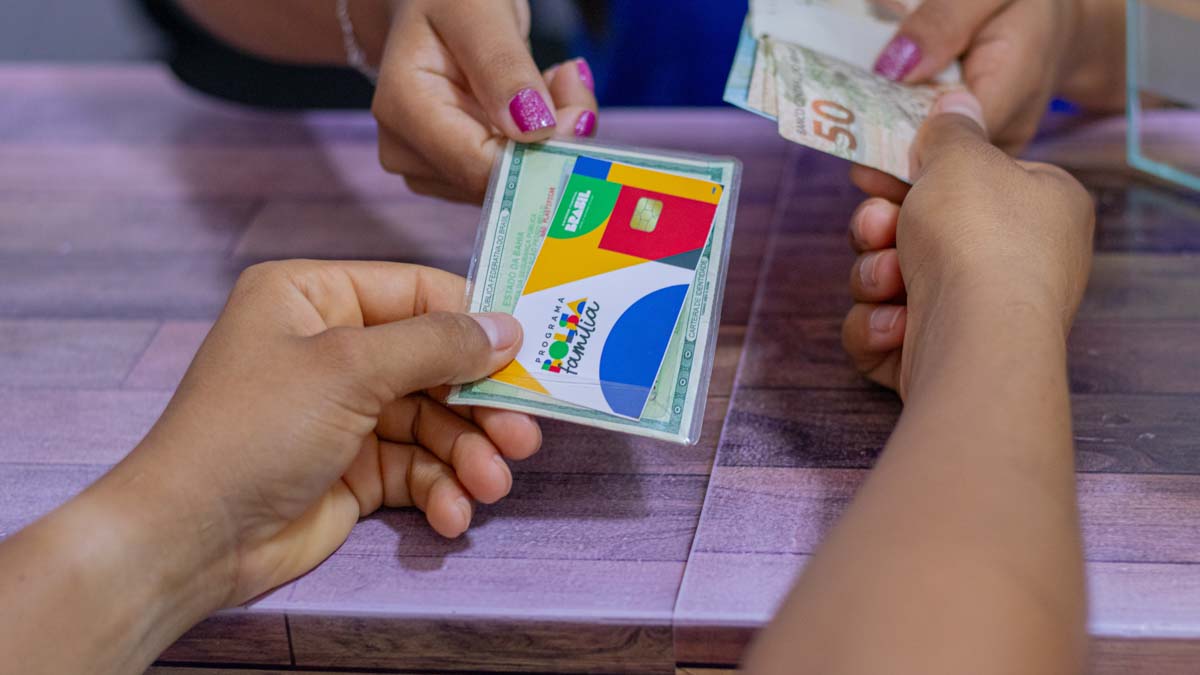 Pessoa recebendo dinheiro do Bolsa Família ao entregar cartão e identidade