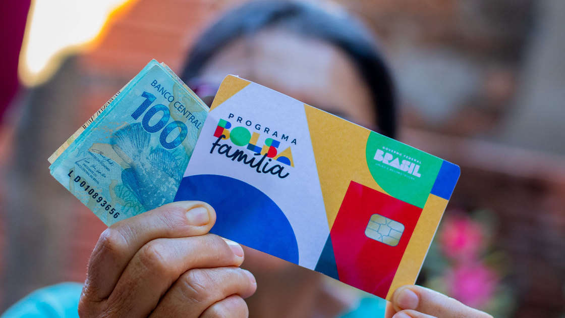 Mulher segurando cartão do Bolsa Família e dinheiro