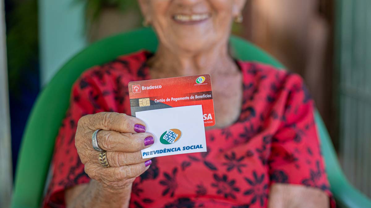 Idosa de mais de 60 anos segura cartão do bradesco de benefício e cartão da previdência social do INSS