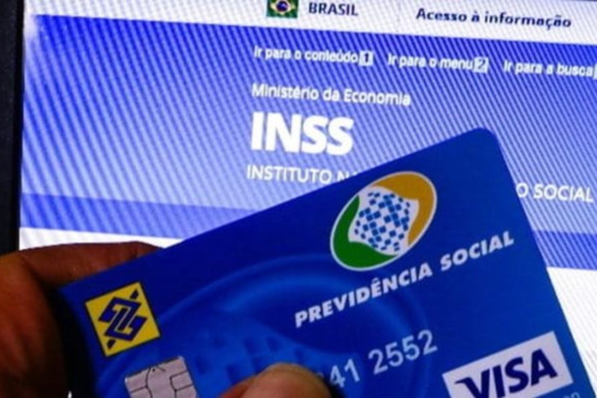 Um home segura seu cartão do INSS em frente ao computador após ver a mensagem de Atenção, aposentados e pensionistas do INSS
