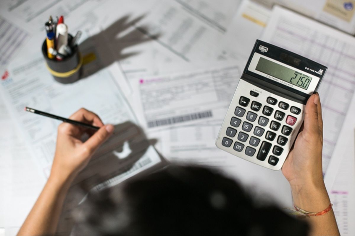 Um homem fazendo um cálculo com um lápis e calculadora após ver a notícia de atenção beneficiários do BPC e Bolsa Família