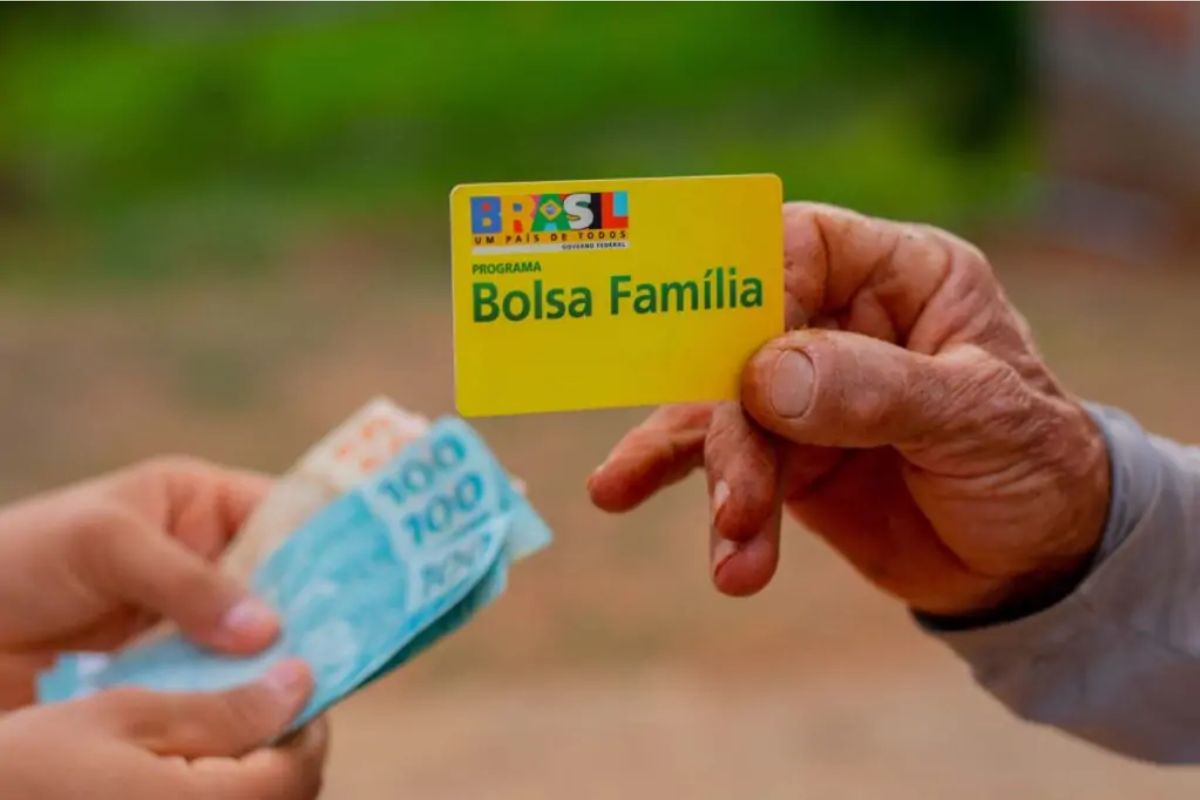 Um homem com o cartão do Bolsa Família pegando dinheiro em outra mão após ver que o Bolsa Família encerra pagamentos do mês de Junho