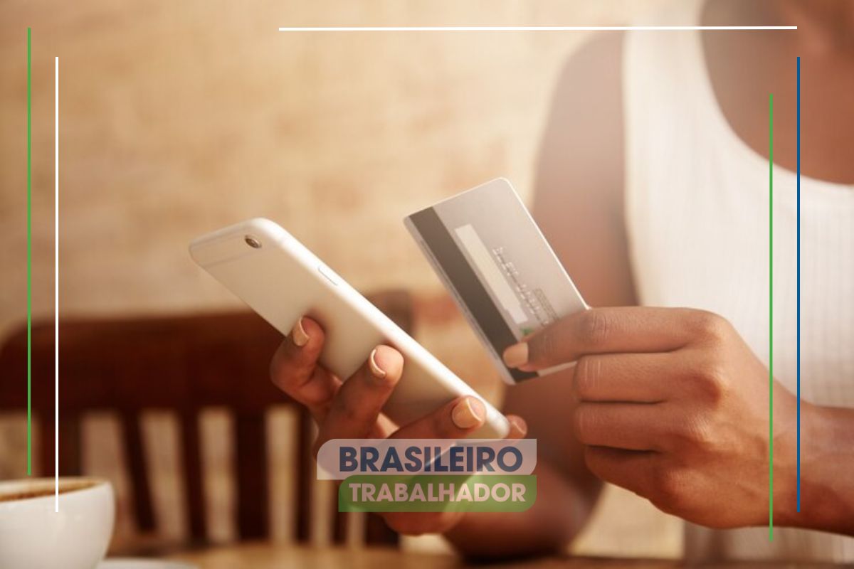 Uma pessoa com seu cartão e celular na mão após ver a disponibilidade do auxílio disponível pela Caixa