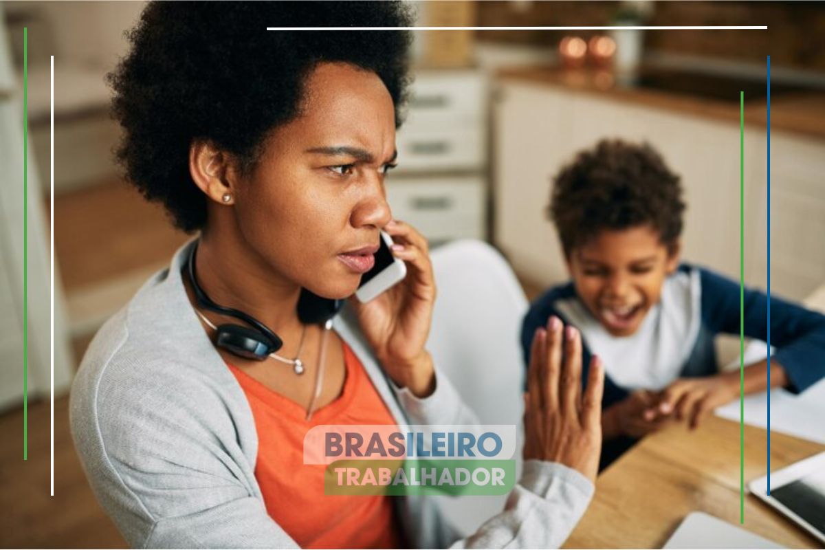 Uma mãe falando ao celular preocupada com o Auxílio Gás. Atrás, o seu filho está sentado em uma mesa