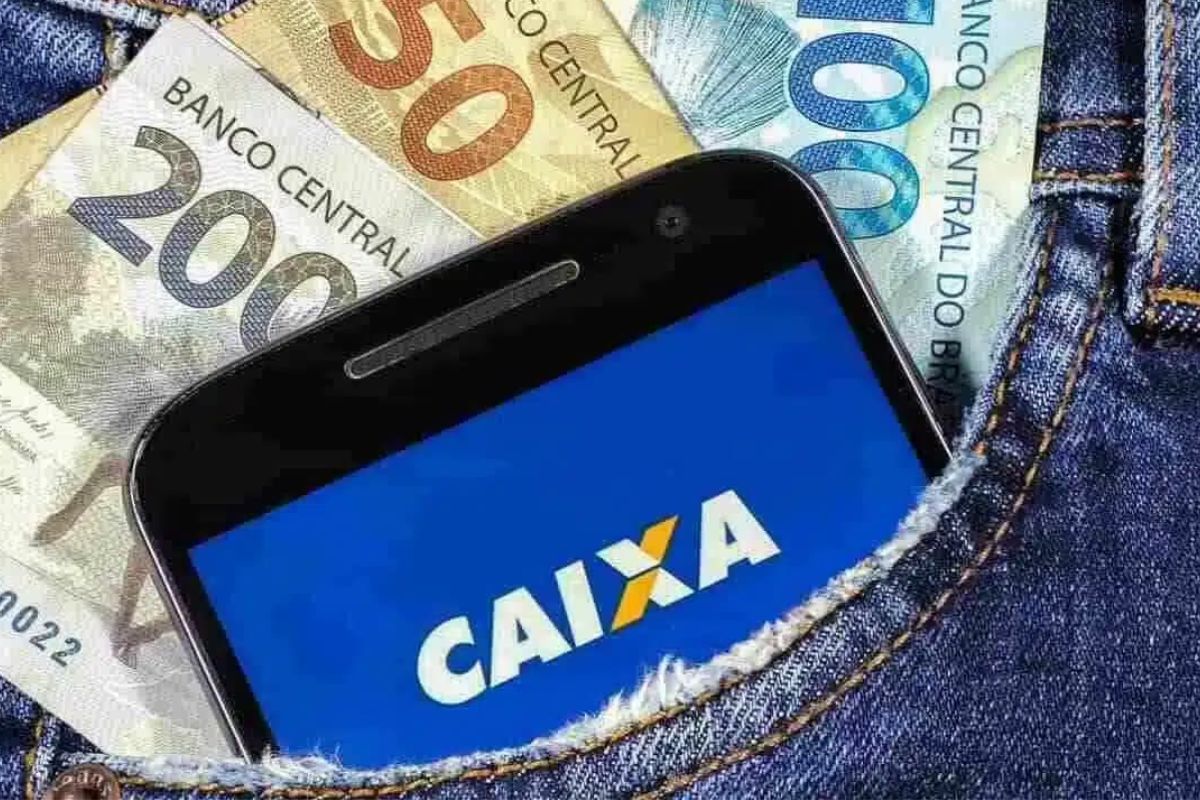 Um homem com o celular e dinheiro no bolso após ver que tem R$ 3 mil disponíveis na CAIXA para CPFs finais 0 a 9