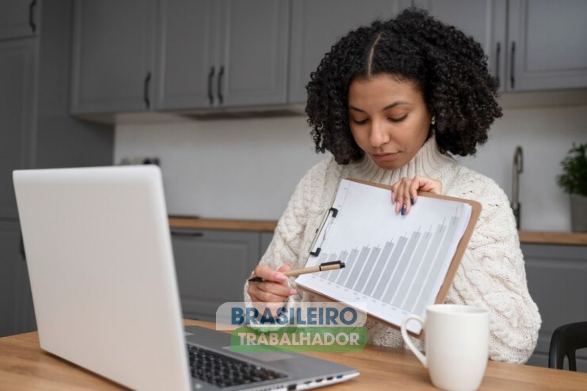 Uma pessoa em frente a um notebook. Ela aponta para um gráfico em sua mão que mostra a alta da Bandeira vermelha na conta de luz