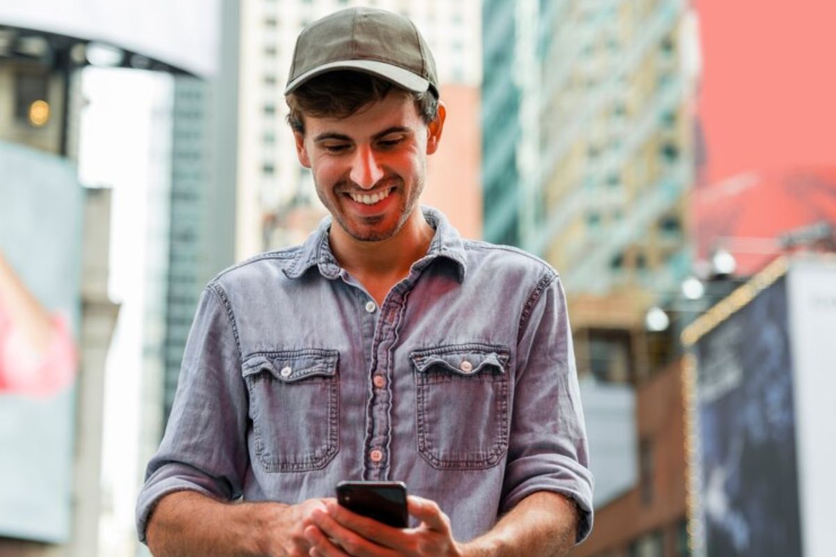 Um trabalhador contente caminha na rua enquanto vê em seu celular que o CAIXA TEM libera R$ 540