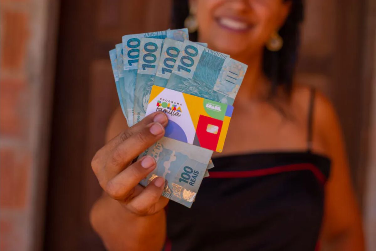 Uma mãe feliz, ela segura o cartão do Bolsa Família e algumas notas de 100 reais após ver os pagamentos de outubro confirmados!