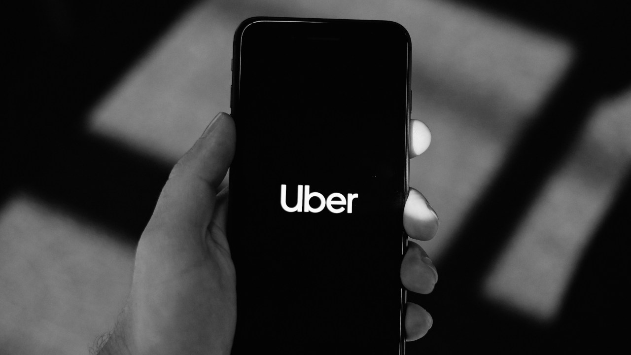 Pessoa com celular na mão e logo da Uber