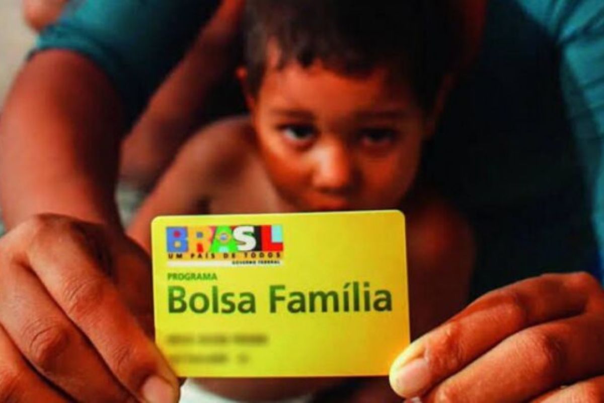 Uma mãe segura o cartão do benefício, seu filho está logo atrás e eles veem que o Governo atualiza critérios do Bolsa Família