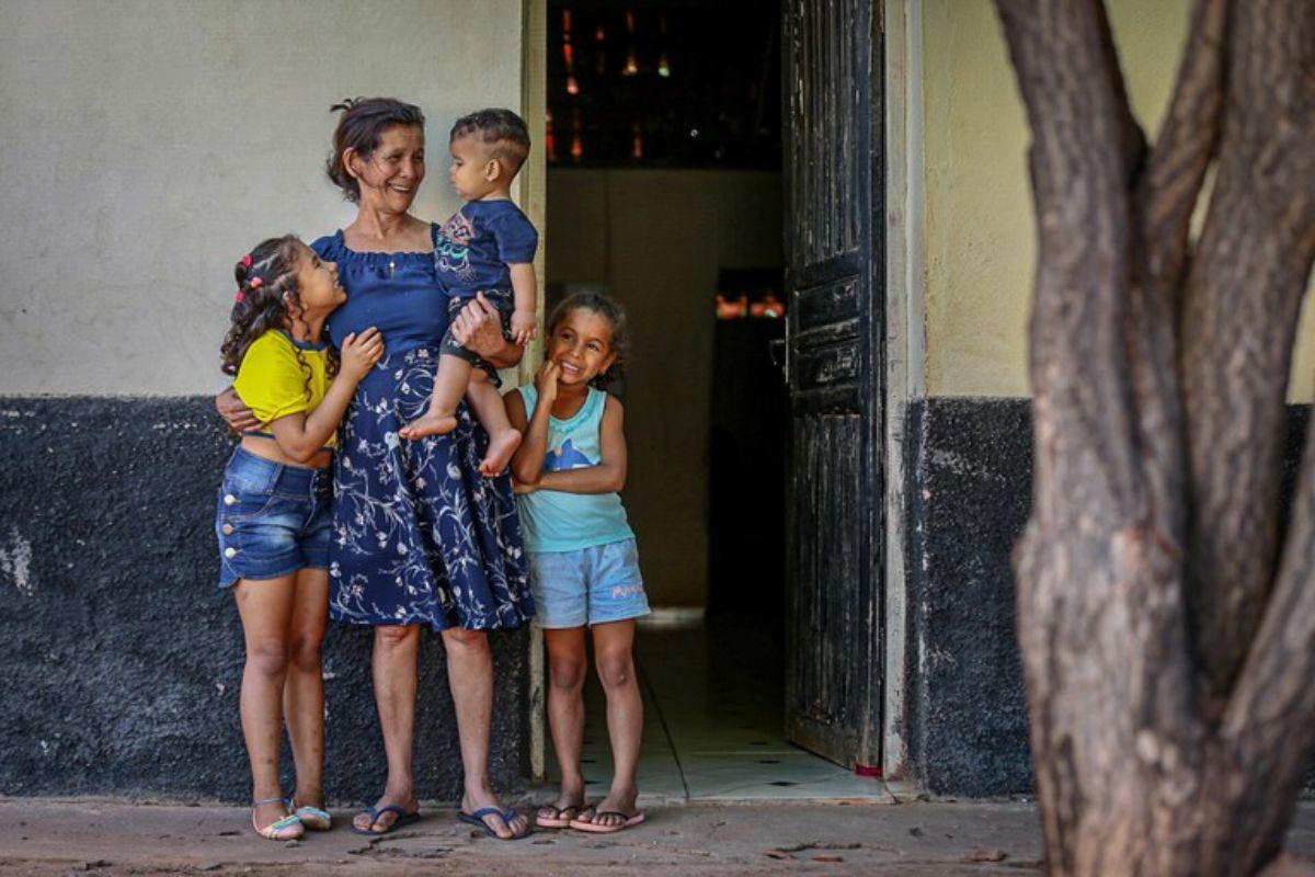 Uma mãe com três filhos em frente de sua casa. Ela sorri aliviada após passar pelo novo corte do Bolsa Família