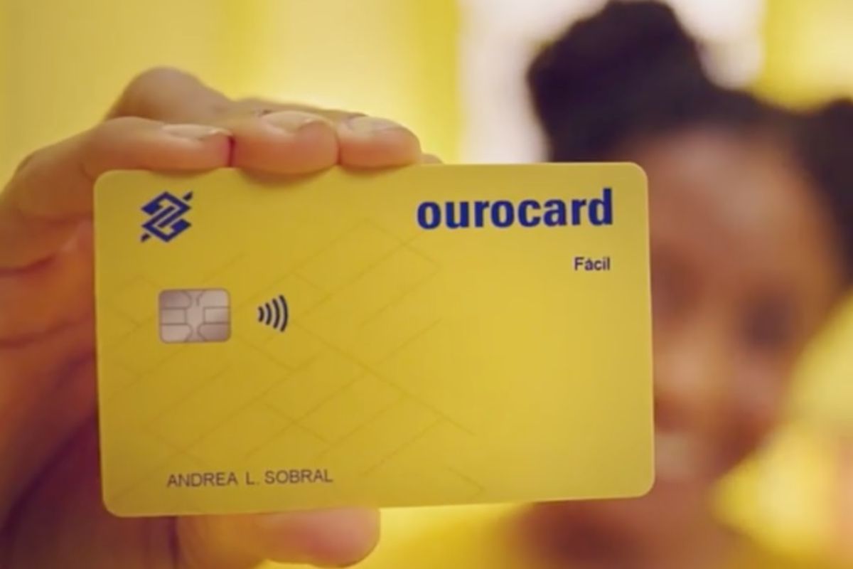 Uma mulher segurando o seu cartão de crédito amarelo, fruto do Pix e Ourocard se unem no Banco do Brasil 