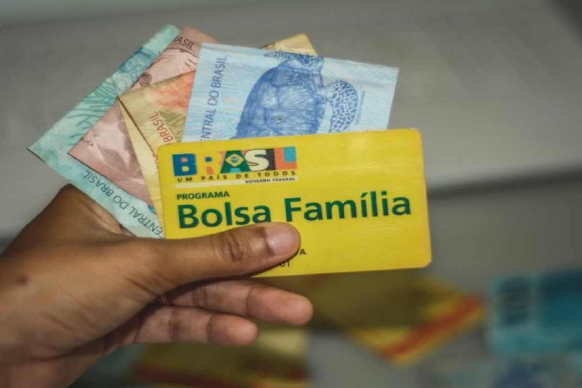 Uma pessoa segura o cartão do Bolsa Família e algumas notas, representando que chegou o Vale-Gás Explosivo com Pix