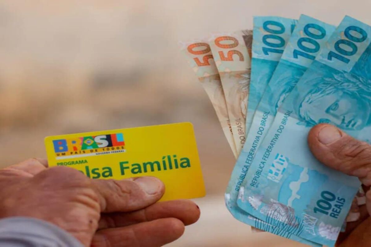 Uma pessoa segurando algumas notas de R$ 50 e R$ 100 e o cartão do Bolsa Família dezembro