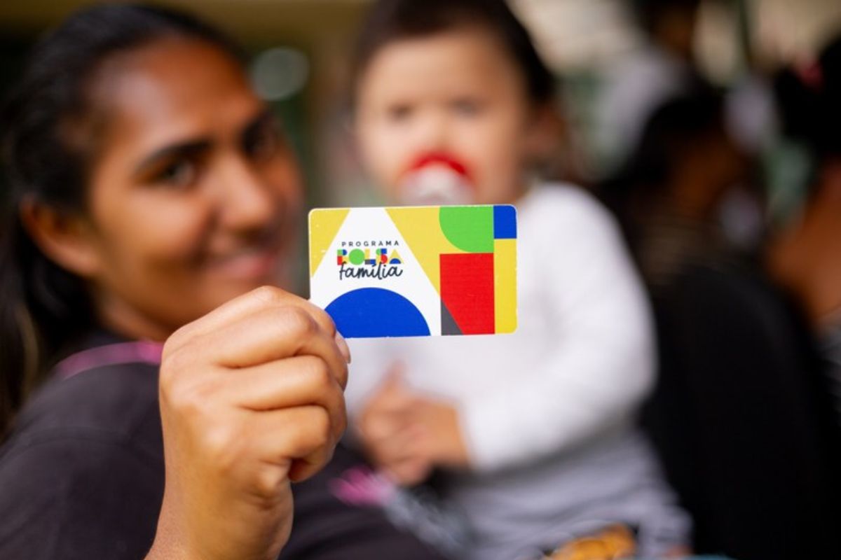 Uma mulher segurando o seu bebê no colo e o cartão e aprendeu Descubra se seu filho tem NIS também