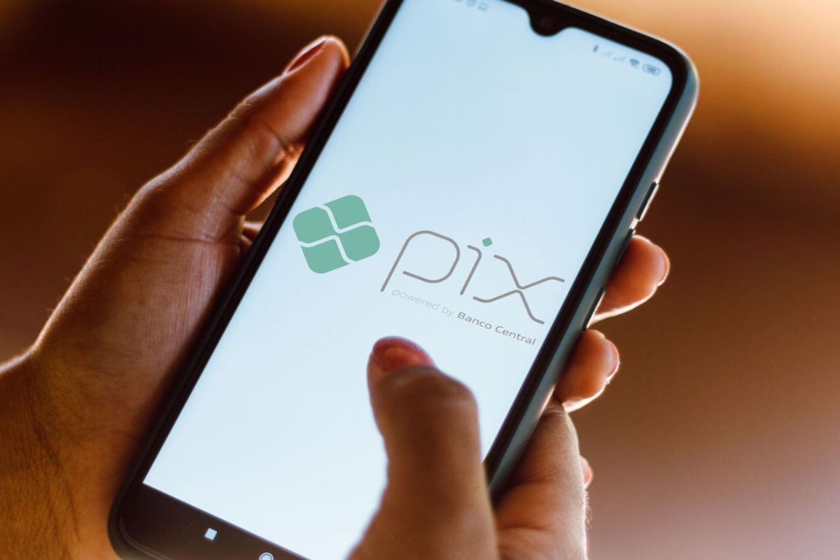 Foco na mão de uma pessoa que segura um smartphone com o símbolo do Pix no celular