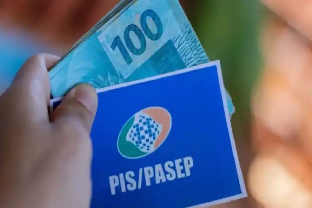 Uma pessoa com o cartão do PIS/Pasep 2025 na mão e outras notas de R$ 100