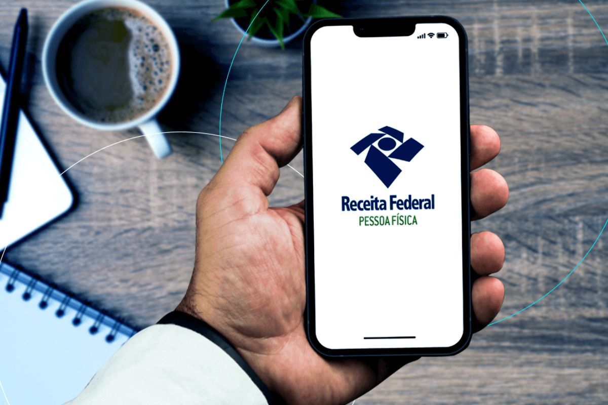 Uma pessoa segura o celular para conferir o calendário de restituição do imposto de renda